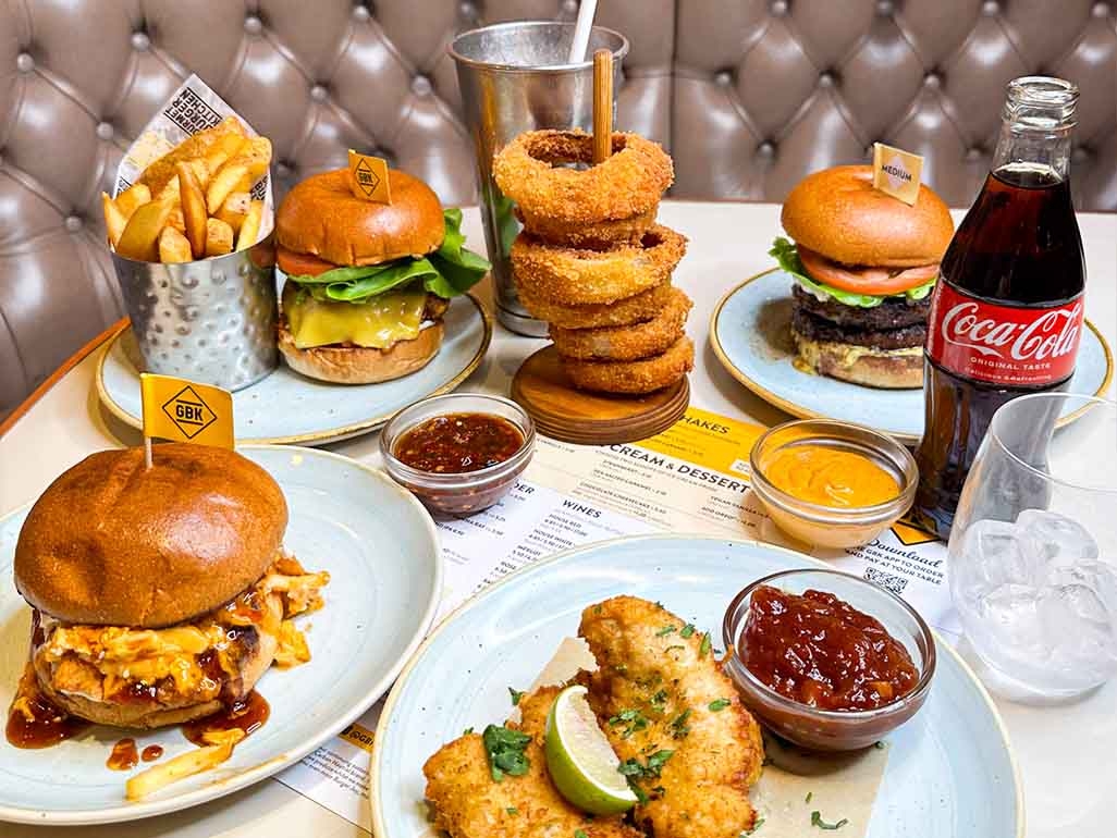 A table of food from Gourmet Burger Kitchen including onion rings, beef burger, bbq chicken burger and fries