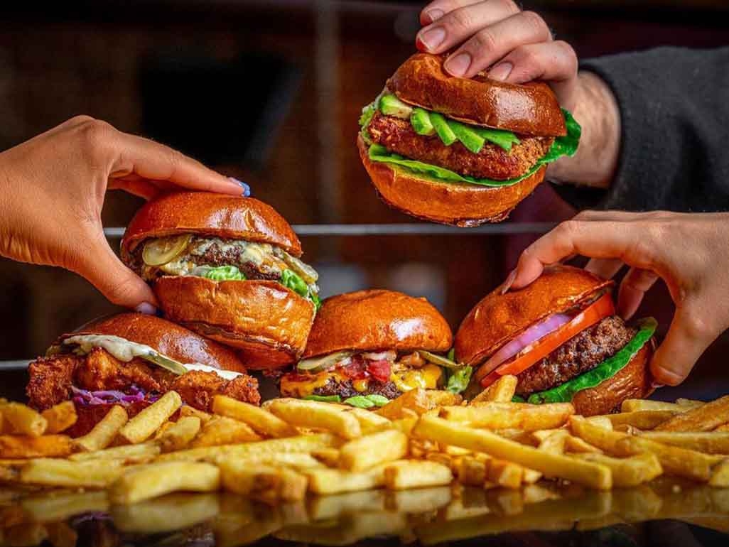 People grabbing beef burgers with avocado, salad, cheese and fries
