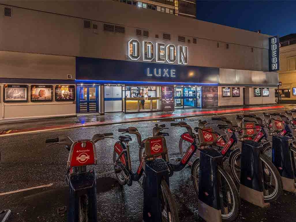 Odeon Luxe at night time with neon lights and electric scooters outside