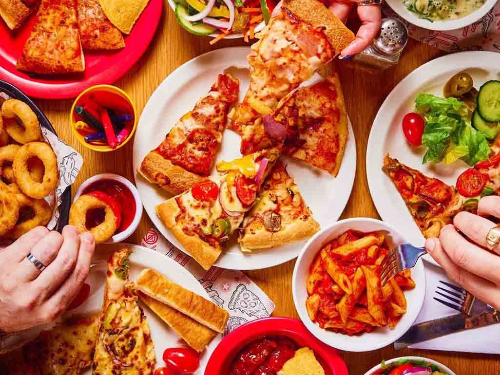 Slices of pizza, pasta, salad and children's crayons.