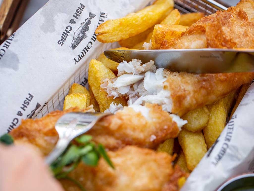 Fish and chips being cut up with a knife and fork